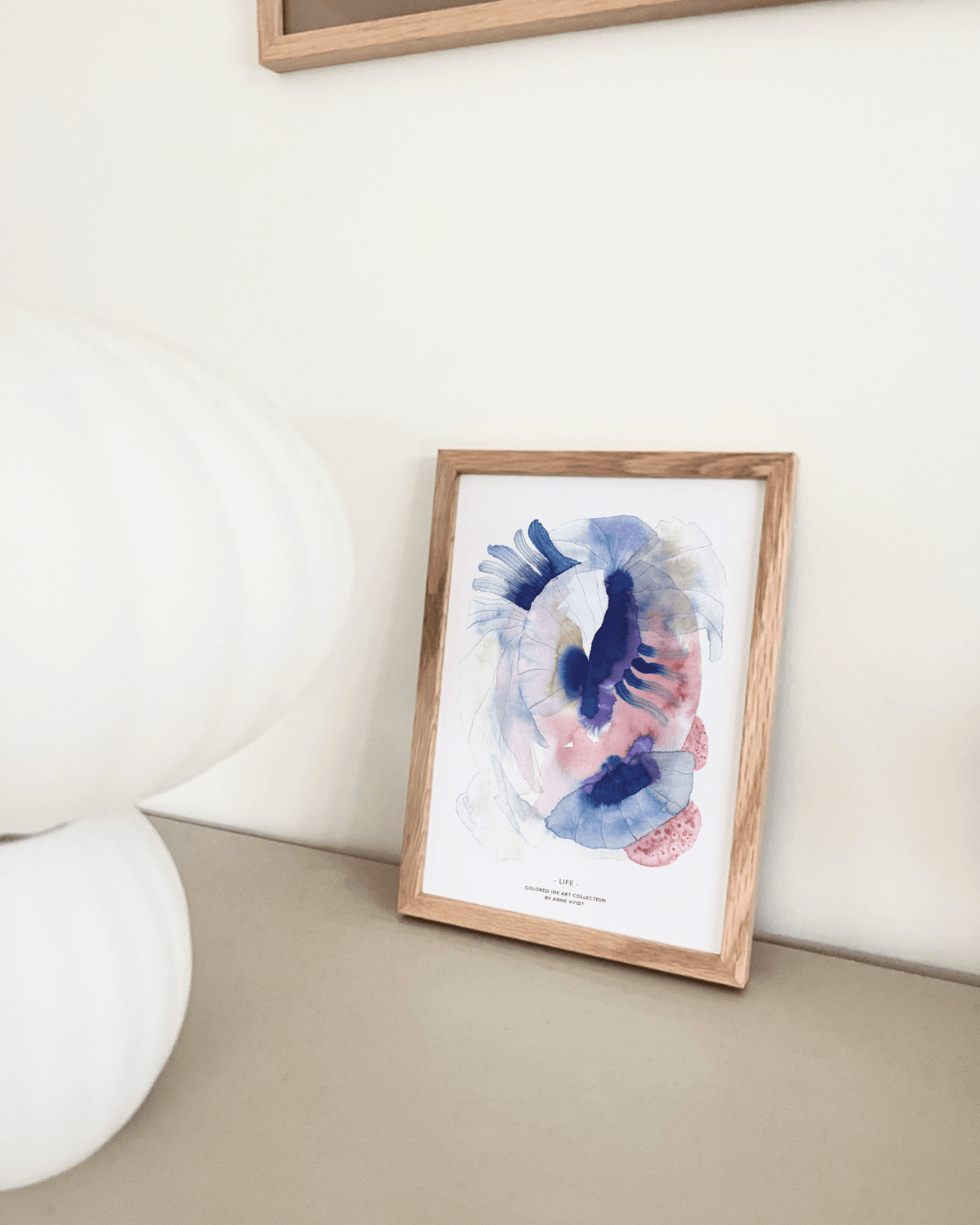 Abstrakt vandfarve motiv i blå og lyserøde farver trykt på a5 kort og sat i ramme i nordisk hjem