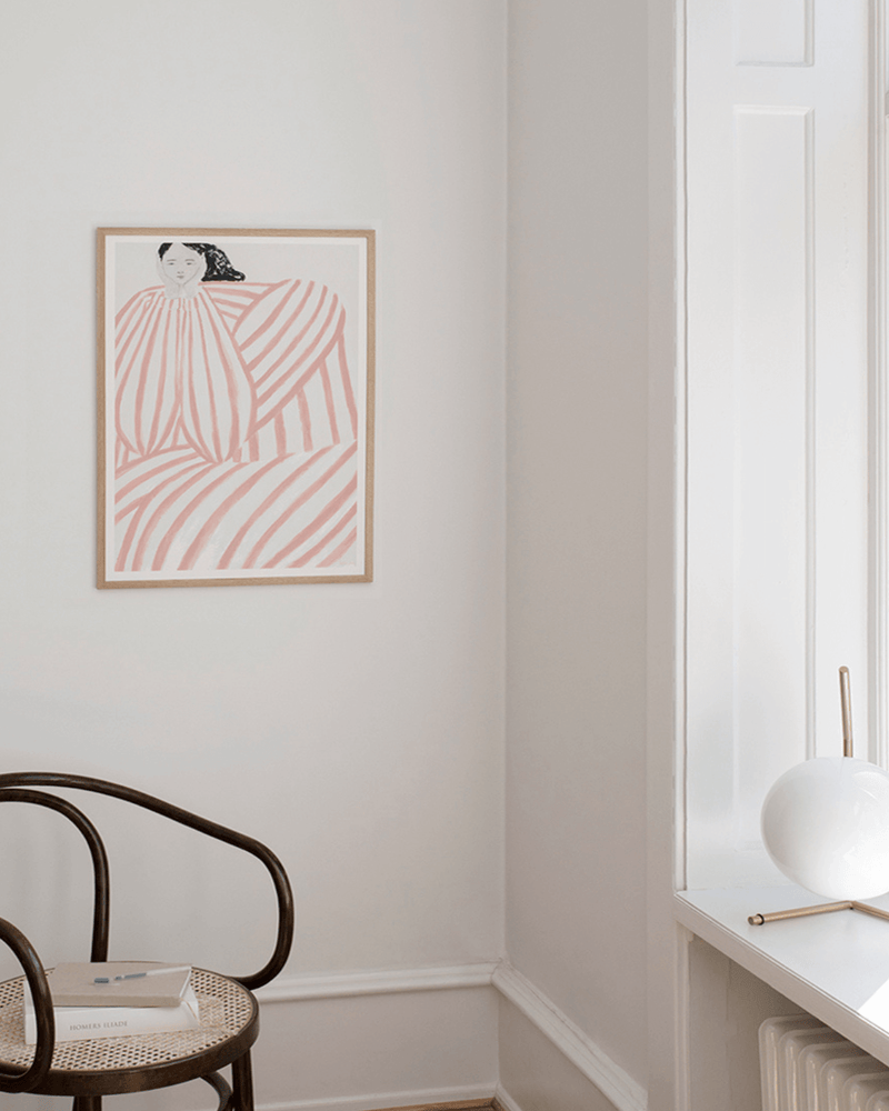 Kunsttryk i egetræsramme på væg i stilfuldt hjem. Kunsttryk med kvinde med sort hår i stribet kjole på lys baggrund- 