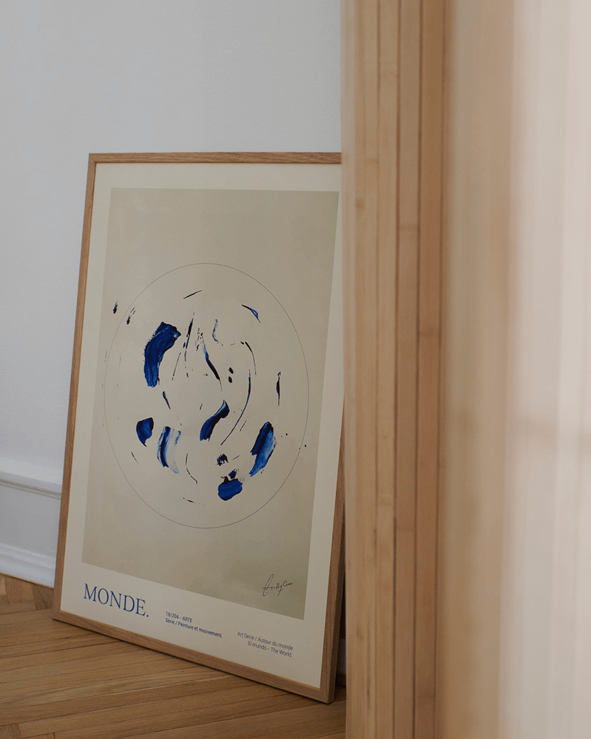 Plakat med malet abstrakt motiv i blå af Lucrecia Rey Caro, indrammet og stående på sildebensgulv. 