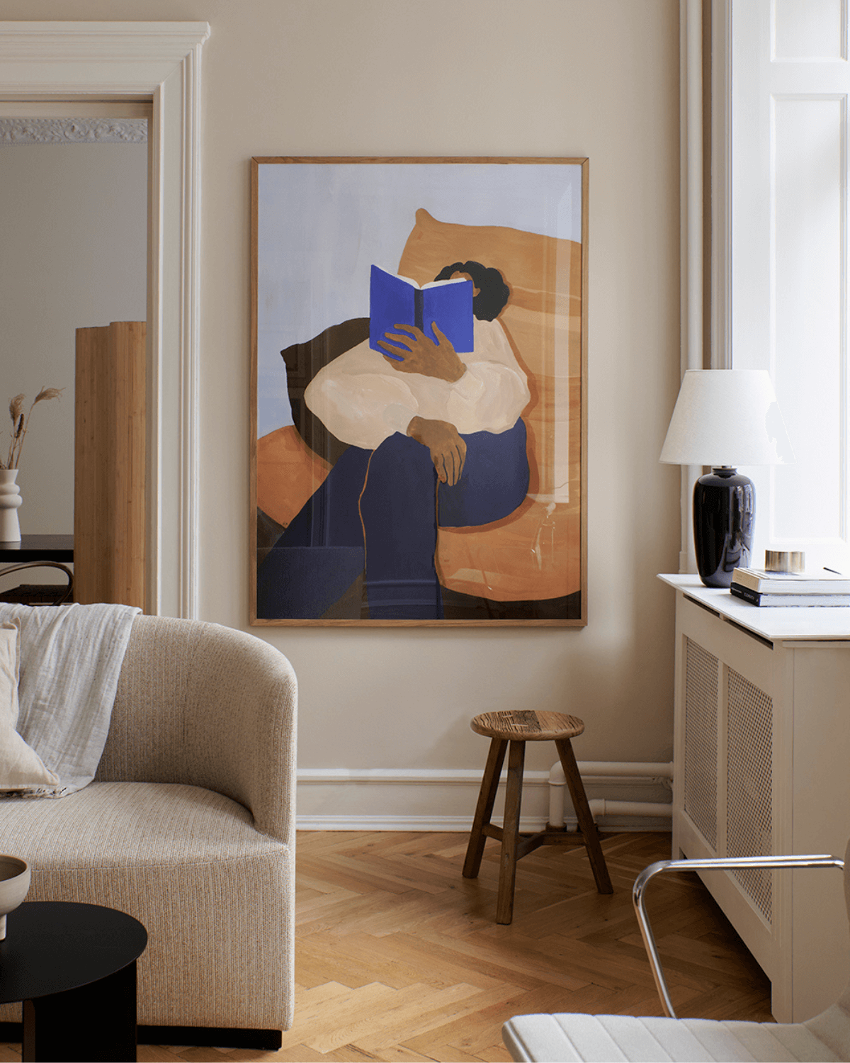 Kunsttryk af læsende kvinde. Indrammet og placeret i rolig beige stue. 