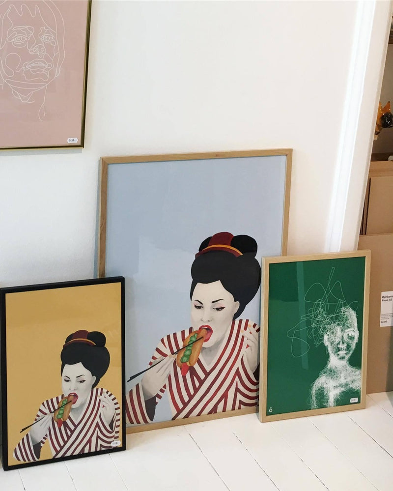 Plakat af Geisha der spiser en hotdog med spisepinde indrammet i egetræsramme 